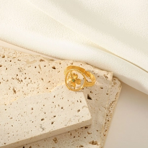 Detailed close-up of golden clover ring with green gemstone on elegant stone texture