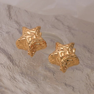 Lustrous gold star-shaped earrings with irregular textured finish on marble background