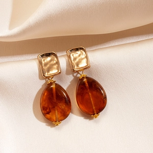 Detailed shot of gold hammered square earrings with amber teardrop charms on beige silk
