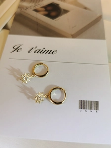 Detail of gold starburst hoop earrings with white zircon on a minimalist French card