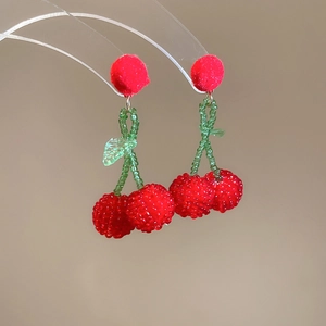 Close-up of handmade cherry earrings with red pom-pom and beaded fruit on a display stand