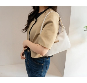 Close-up of a white lychee grain leather underarm bag with gold metal buckle on model