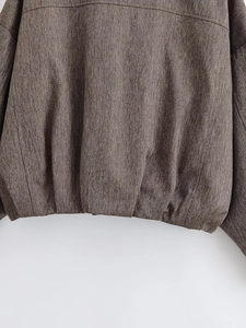Close-up of dark brown herringbone fabric texture and hem sewing on bomber jacket