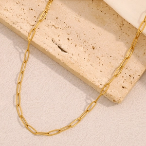 Close-up of golden paperclip link chain on textured beige stone with white satin fabric