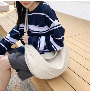 Large beige crescent nylon bag worn as a shoulder bag on a natural wooden stairs background