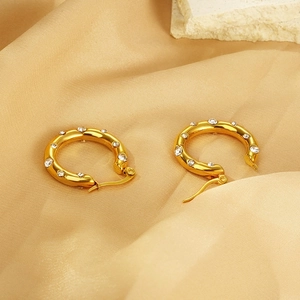 Detailed macro view of gold-plated U-shaped earrings with inlaid rhinestones on silk