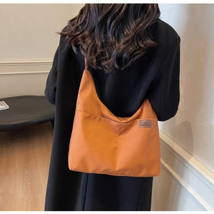 Close-up of a large orange-brown canvas hobo bag worn with a black coat for daily use
