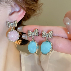 Detail view of pink and blue bow resin earrings with silver needles on model and hand