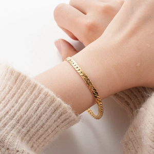 Close-up of a gold flat herringbone snake chain bracelet worn on a female wrist