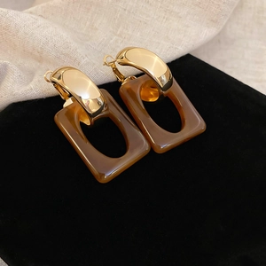 Detail view of amber resin geometric earrings with gold metal accents on black velvet