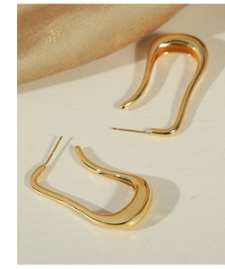 Close-up of golden wavy U-shaped earrings on light textured surface with silk cloth