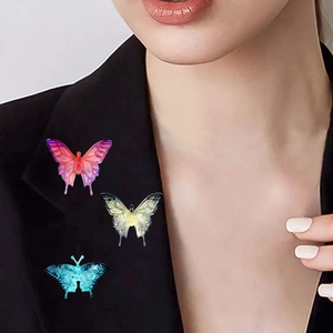 Trois broches papillon colorées en rose, jaune et bleu sur une veste de blazer noire