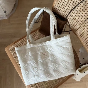 Close-up of shell-shaped quilted texture and fabric label on white puffer tote bag