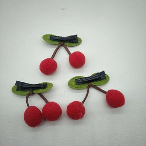 Detail view of cherry hair clips with red pompoms, green felt leaves and metal duckbill clips