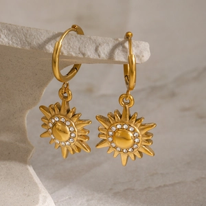 Elegant gold celestial sun pendant earrings with sparkling zircons on stone display