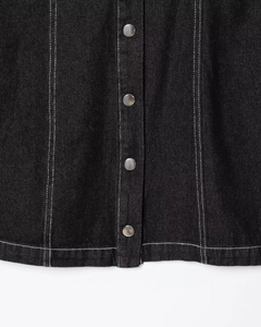 Detailed view of black denim fabric featuring white contrast stitching and silver metal buttons