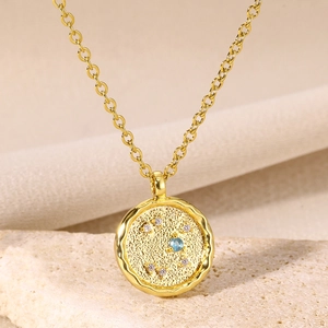 Macro detail of 18K gold zodiac necklace pendant with blue gemstone and coin texture