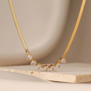 Gold herringbone chain necklace with seven teardrop-shaped zircons on stone background