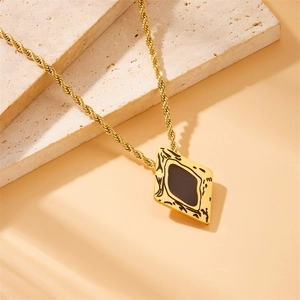 Detail of a gold twist chain necklace featuring a diamond-shaped black stone pendant