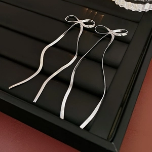 Détail de boucles d'oreilles nœud argenté avec de longues chaînes serpent sur plateau
