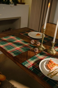 Detailed view of red and green plaid table mat on dark wood with holiday decor