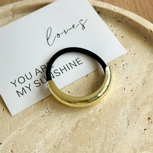 Close-up of a minimalist golden curved metal hair tie on a decorative stone tray