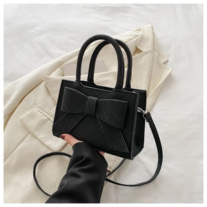 Detail of black mini handbag with oversized bow and herringbone texture on white fabric