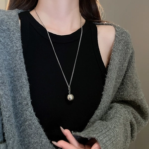 Detailed view of a polished silver ball pendant necklace worn on a simple metal chain