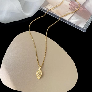 Macro detail of a gold leaf pendant with inlaid crystals on a beige pebble cushion