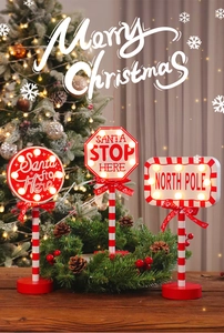 Close-up of LED Christmas Santa Stop Here road signs with festive pine cones and lights