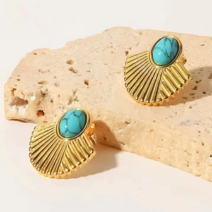Macro shot of gold fan-shaped stud earrings with turquoise inlay on natural stone props