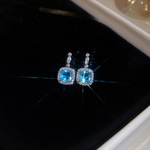 Macro shot of silver square sea blue gemstone earrings with diamond halo on black velvet