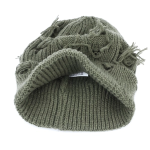 Macro detail of olive green distressed knit beanie showing ripped texture and wash label
