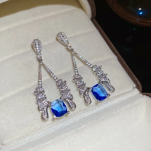 Close-up of silver dangle earrings with micro-pave zircons and blue cushion-cut gemstones