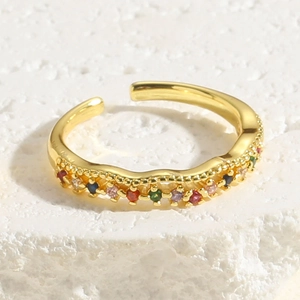 Close-up of golden adjustable ring with wavy texture and colorful zircon stones on stone