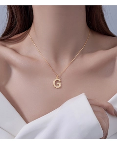 Close-up of a gold-toned necklace featuring a micro-set letter G pendant on a model