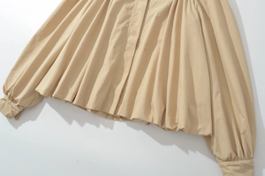 Détail des manches bouffantes et de l'ourlet plissé sur un haut tissé beige chic