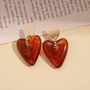 Macro detail of heart-shaped acrylic resin earrings in amber brown with golden metal studs