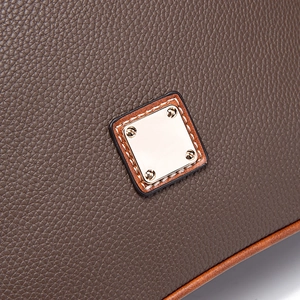 Detailed close-up of golden metal plate on brown pebble leather crossbody bag with stitching