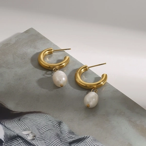 Elegantes pendientes en C dorados con colgantes de perlas blancas sobre revista