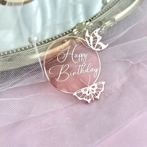 Detail of round pink acrylic birthday cake topper with butterflies on pink tulle