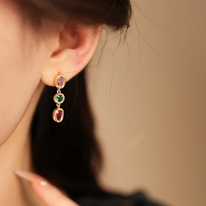 Detail von Vintage-Goldohrringen mit lila, grünen und roten ovalen Edelsteinen am Modell