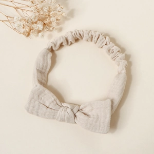 Close-up of beige muslin cotton baby headband with a soft bow and elastic texture