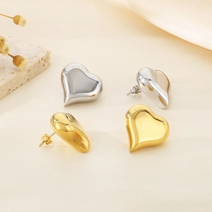 Close-up of gold and silver heart-shaped stainless steel earrings on a beige fabric