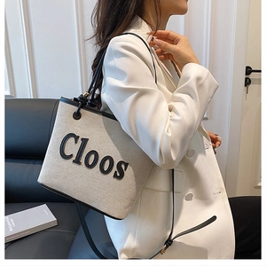 Detail of off-white canvas tote bag with black leather trim and Cloos logo branding