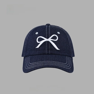 Close-up of white bow embroidery detail on a dark blue denim baseball cap