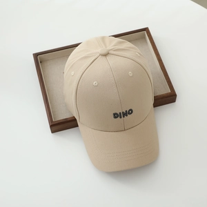 Close-up of DINO letter embroidery on a khaki cotton baseball cap in a wooden tray
