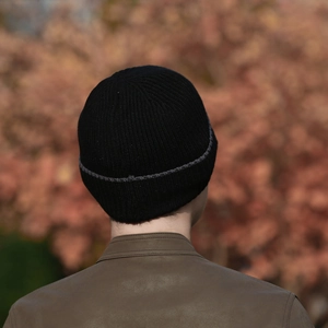 Winter black rib-knit beanie with grey stripes worn by model in an outdoor autumn setting