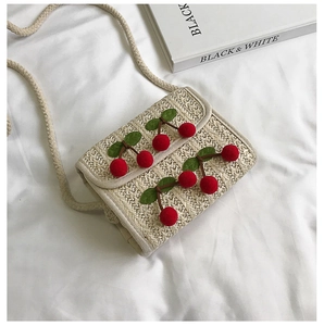 Detail of hand-woven straw crossbody bag with 3D red cherry accents on white fabric