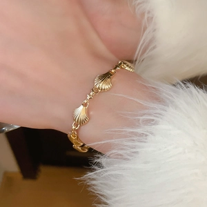 Detailed view of a gold shell bracelet worn with a white cozy winter sweater cuff